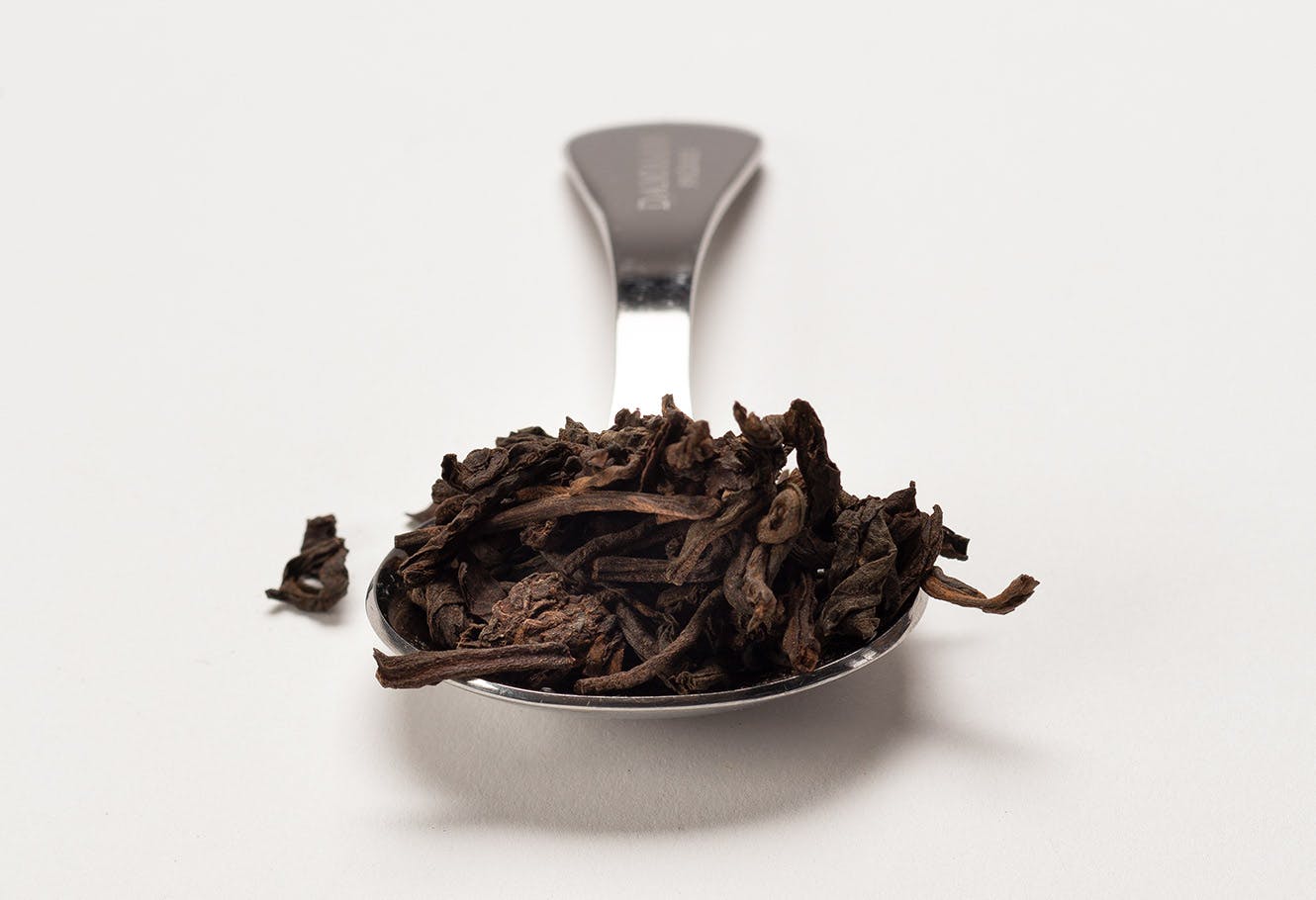 Cuillère à mesurer en acier inoxydable avec du thé sombre en vrac.